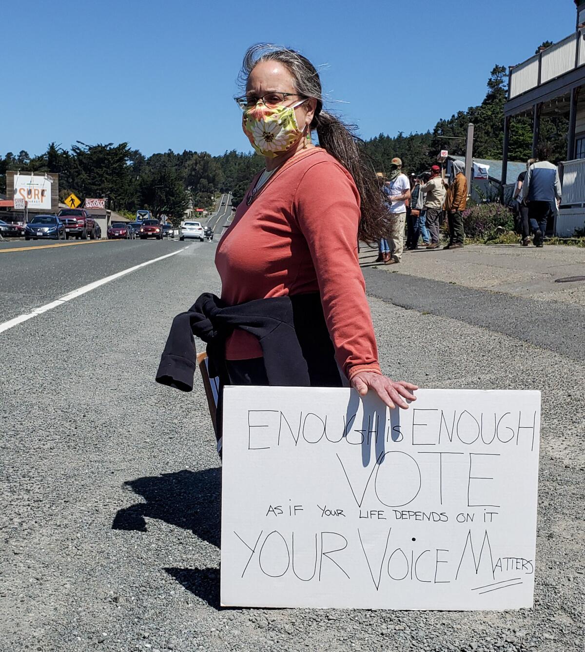 Lisa Joakimides takes a knee with her homemade sign during a George Floyd protest along Highway 1 in Gualala, Calif. 