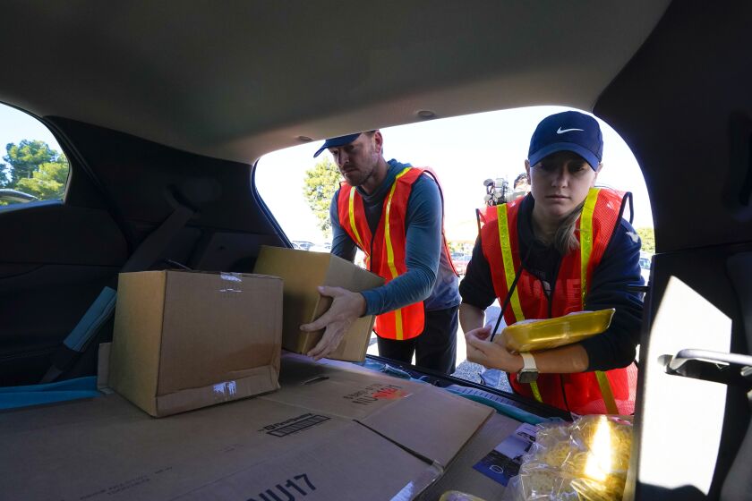 Chula Vista, CA - December 20: Hundreds of cars at the drive-through food distribution event hosted by the Feeding San Diego at Southwestern College on Tuesday, Dec. 20, 2022 in Chula Vista, CA. Quinci Howard (r) and Jordan Weir (l) were among the volunteers who loaded vehicles with 40 pounds of food. Each car was given a box of non perishable, frozen chicken, fresh produce and cheese. (Nelvin C. Cepeda / The San Diego Union-Tribune)