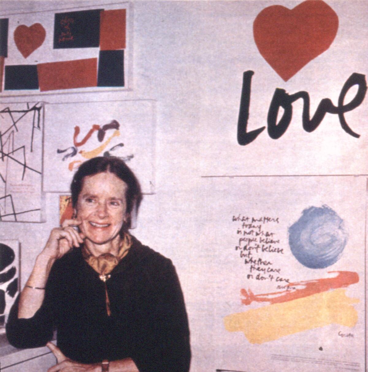 A woman sits and smiles in front of colorful prints, including one that reads "LOVE"