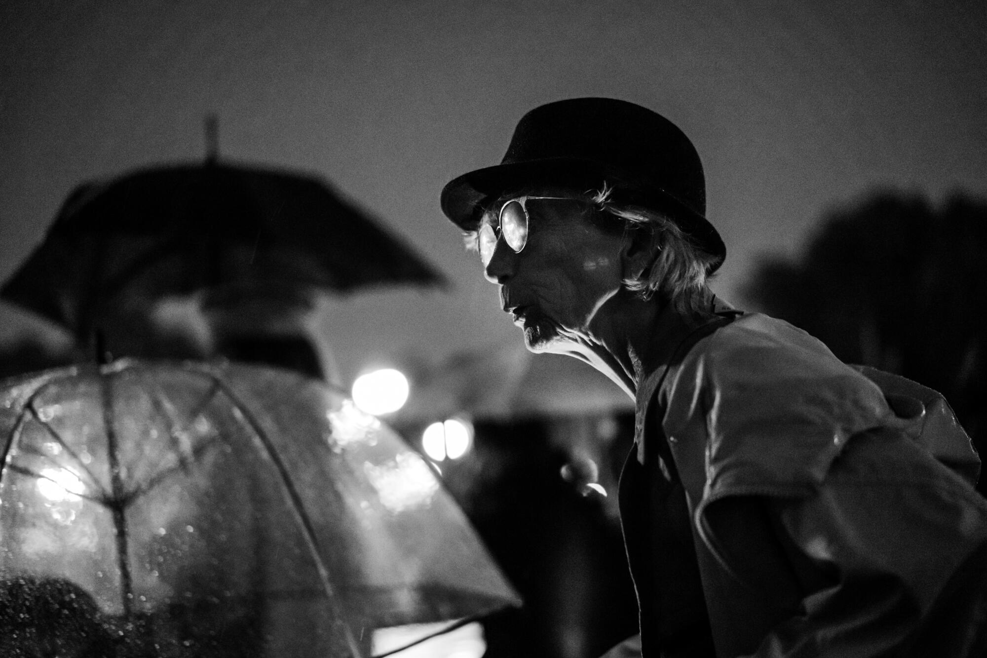 A woman in glasses peers past people holding umbrellas.