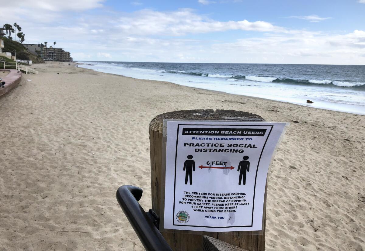 A sign emphasizing social distancing is posted at a virtually deserted Main Beach in Laguna Beach.