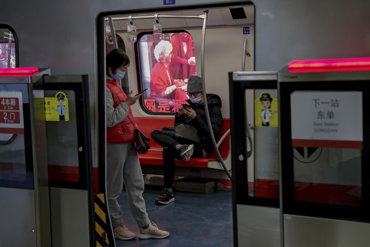 Commuters on a subway train wear masks as they look at their cellphones