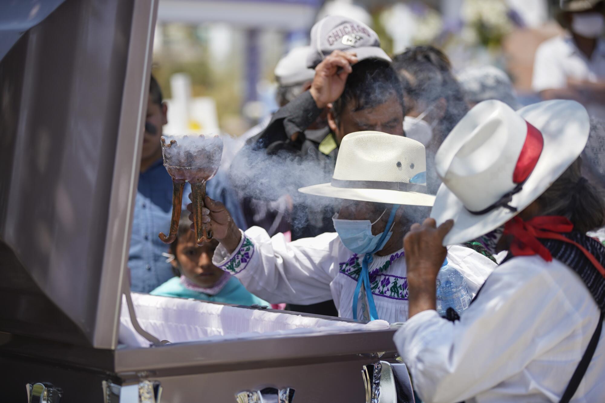 A woman holding an urn filled with incense prays over the open casket of Maria Eugenia Chavez Segovia.