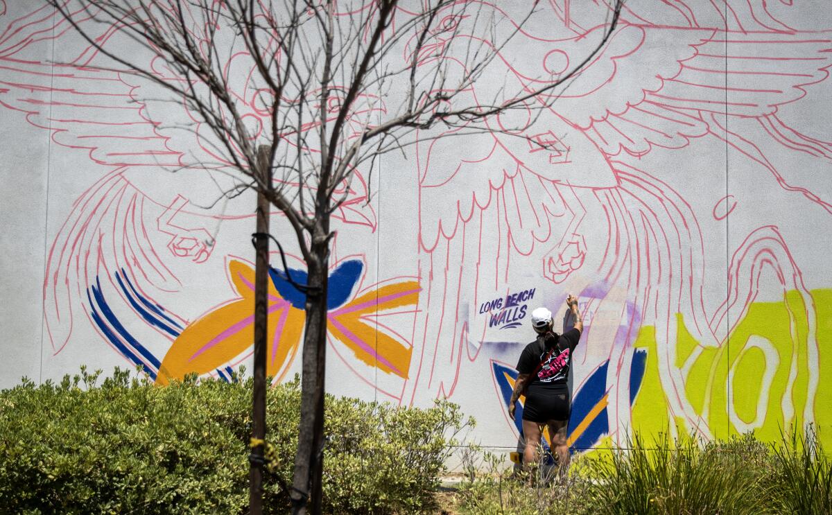 Long Beach Walls artist Stevie Shao sprays paint on a mural in progress on a building.