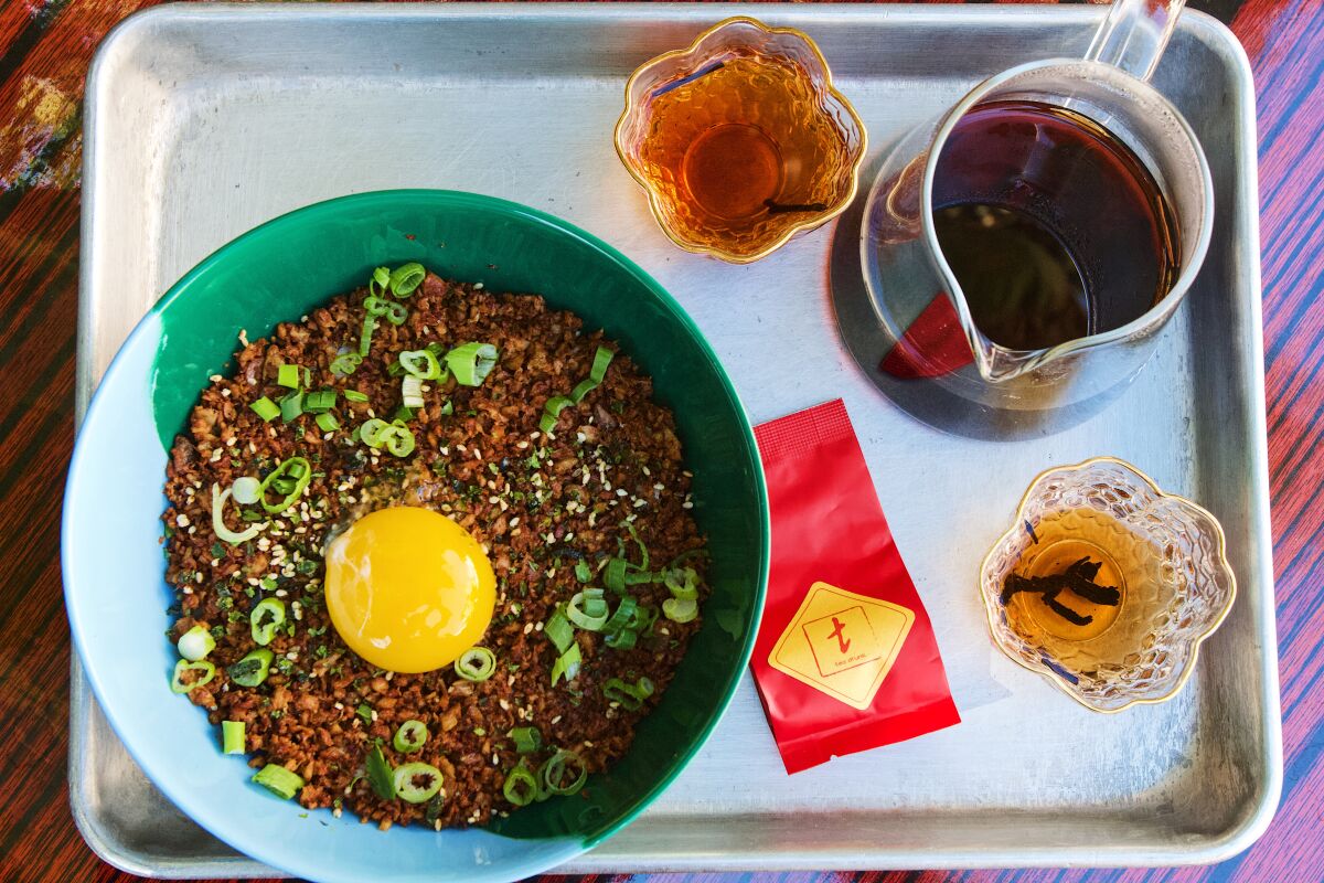 Une vue aérienne d'un plateau avec du thé et un bol de riz au poulet fumé surmonté d'un jaune d'oeuf