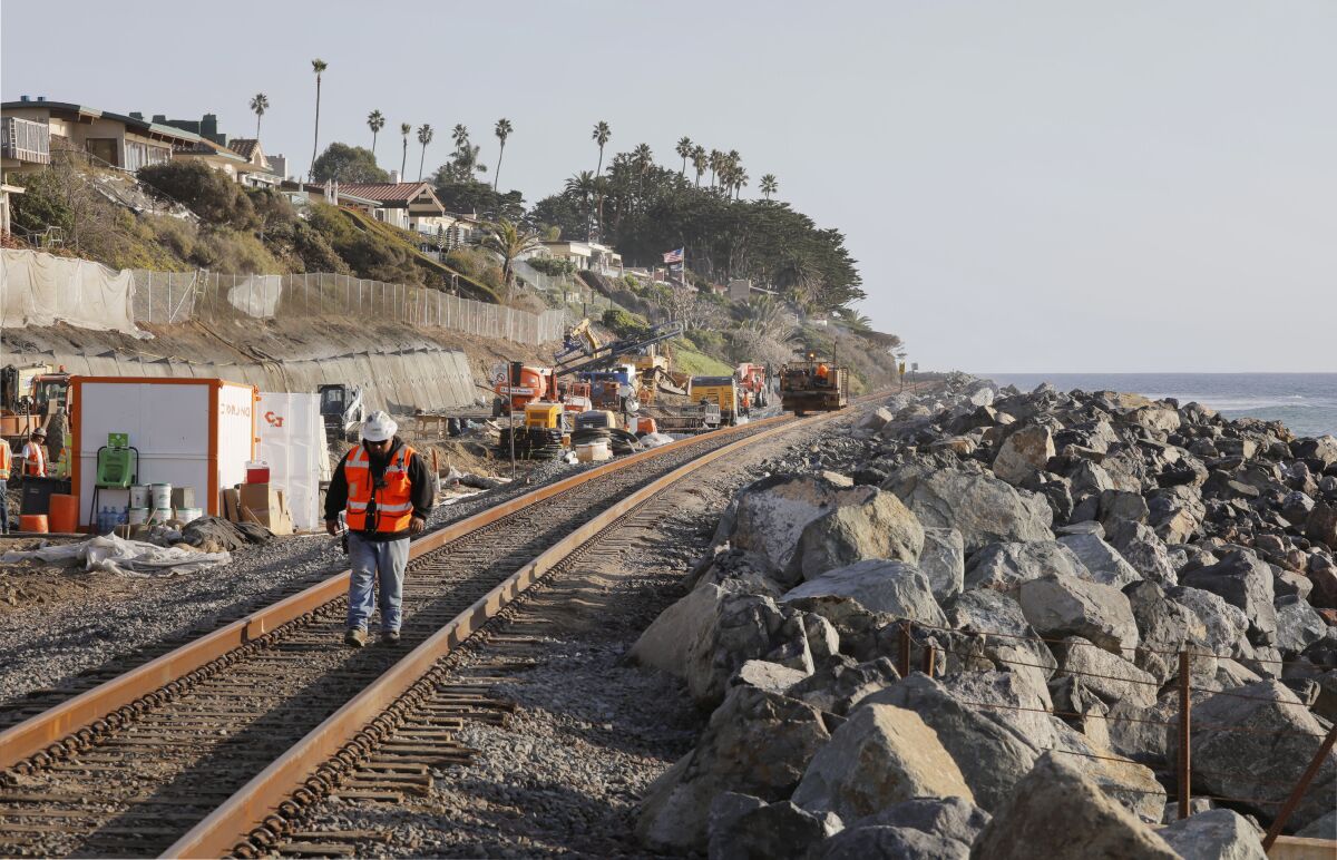 Heavy machinery next to coastal train tracks separated from the ocean by large boulders