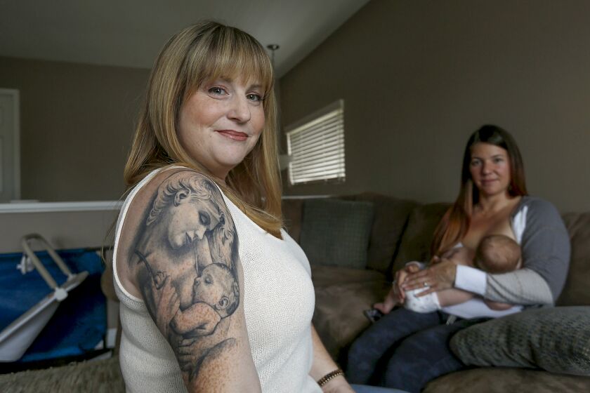 Registered nurse and lactation consultant Rachelle King proudly shows her mother and baby tattoo while client Kaitlyn Ramos breast feeds son Bowen during a home visit in Rancho Santa Margarita on Thursday.
