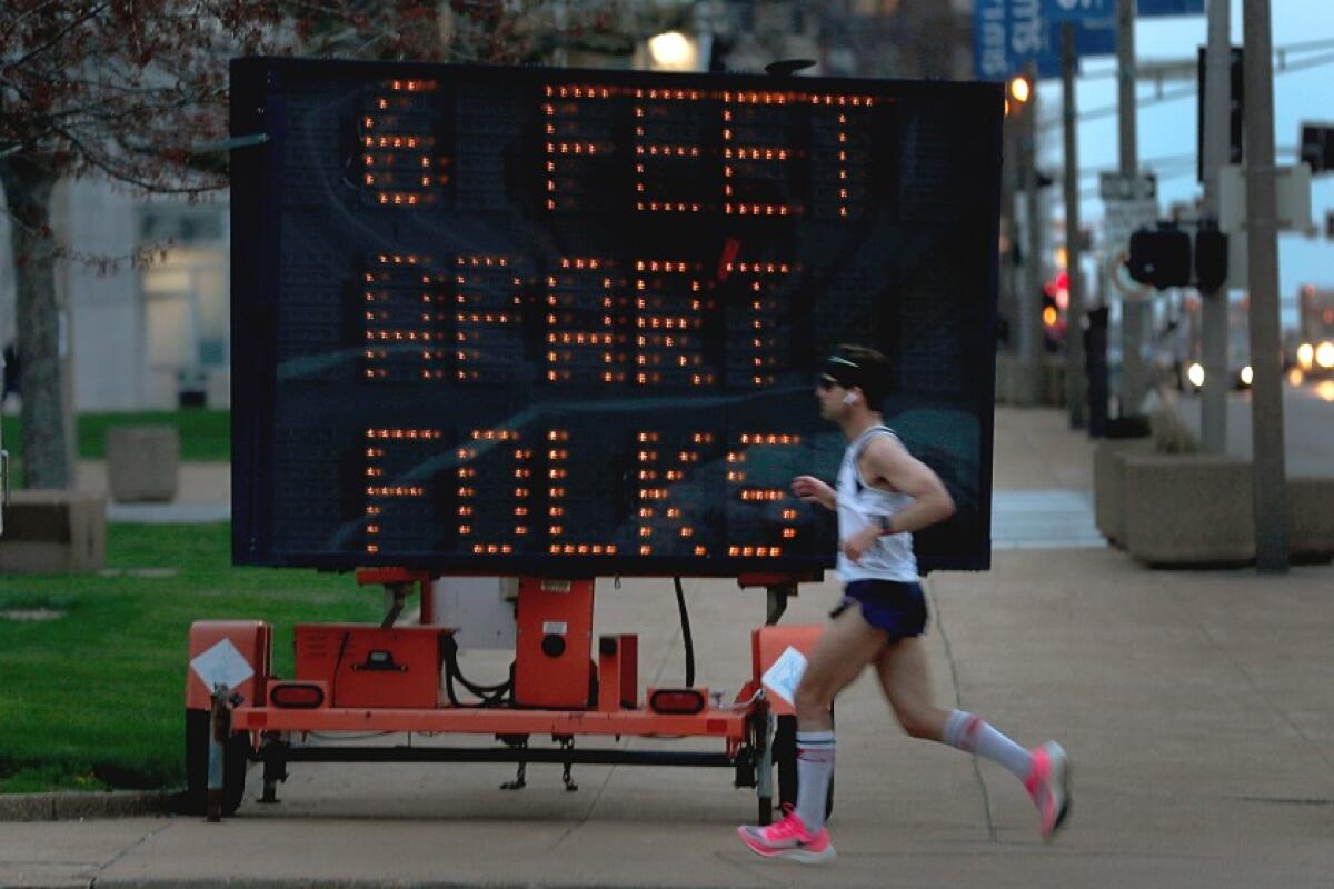 A jogger runs before a lighted sign that says "6 feet apart folks."