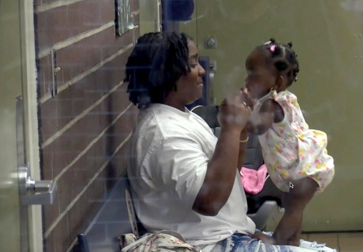 A mother sitting on a bench and holding her child's hands as the child stands on her lap.