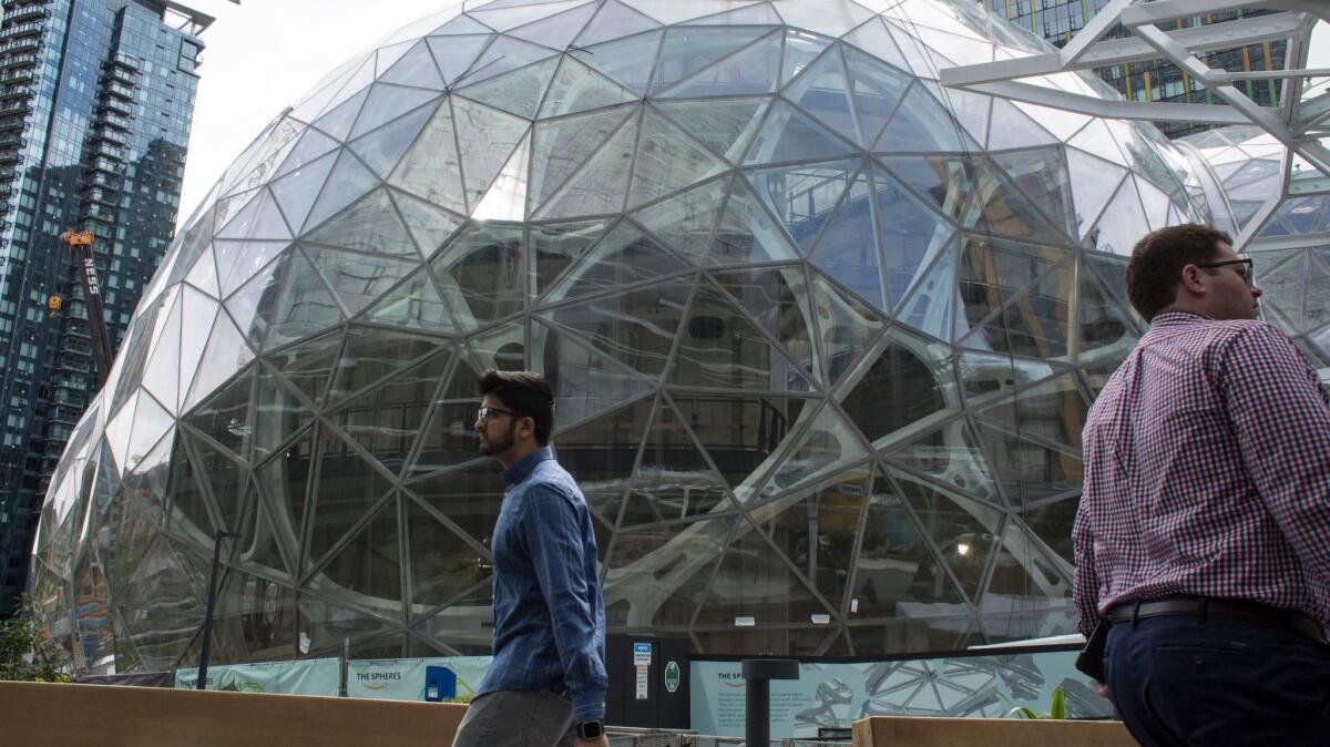People walk past the signature glass spheres under construction at the Amazon corporate headquarters in Seattle. The online giant will decide next year which metropolitan area will be the site of its second headquarters.