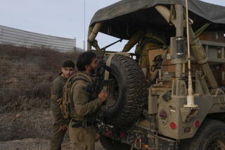 Israeli soldiers stand next to a military vehicle