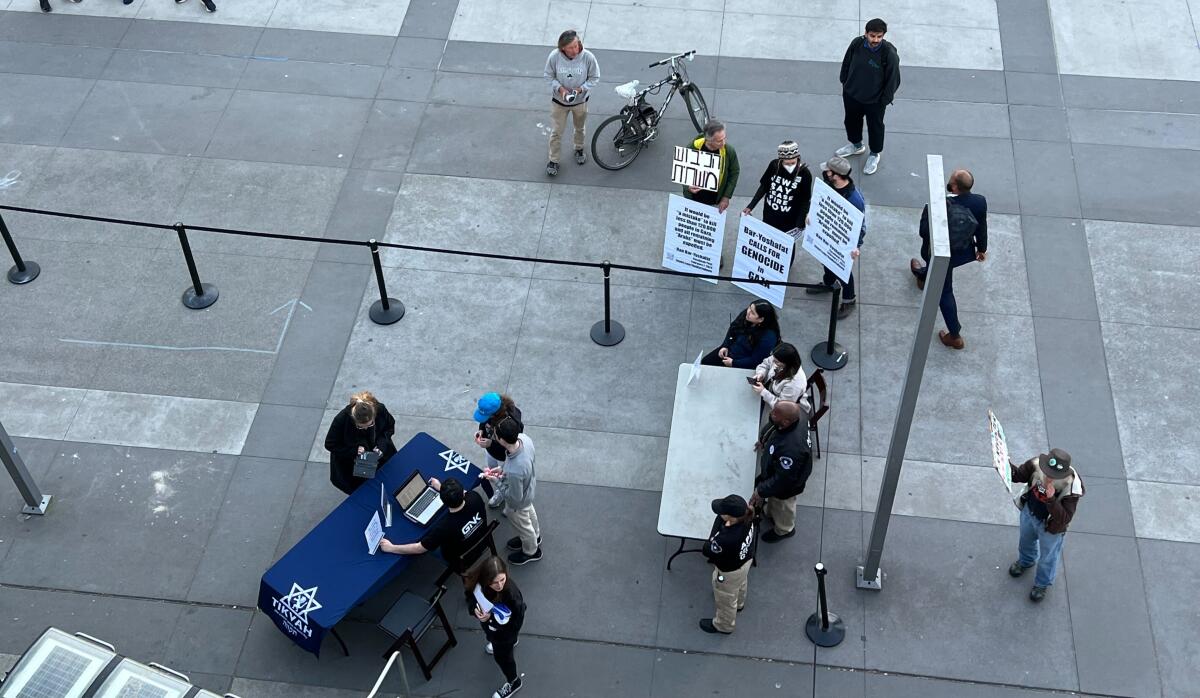 A few people holding signs stand near tables on a college campus.