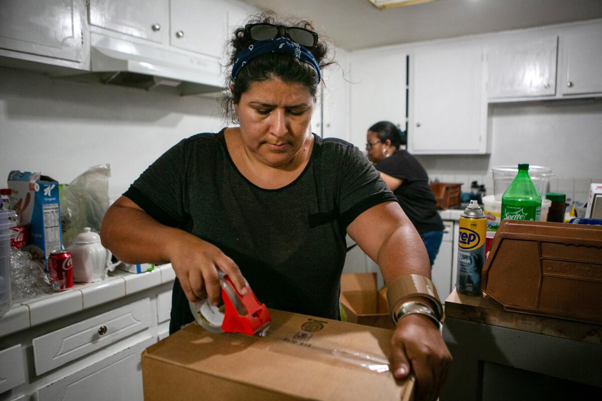 A woman tapes a cardboard box as she packs up her kitchen.