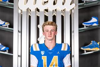 Quarterback Henry Hasselbeck stands in a UCLA football uniform in front of a UCLA sign