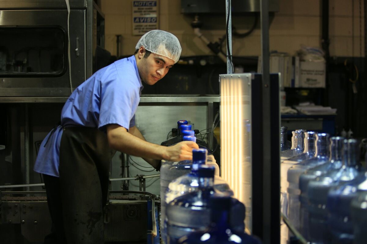 Palomar Mountain Premium Spring Water employee Luis Villarreal guides five gallon jugs of water in front of an inspection light. The water is brought to the bottling station by truck from a spring on Palomar Mountain. — David Brooks