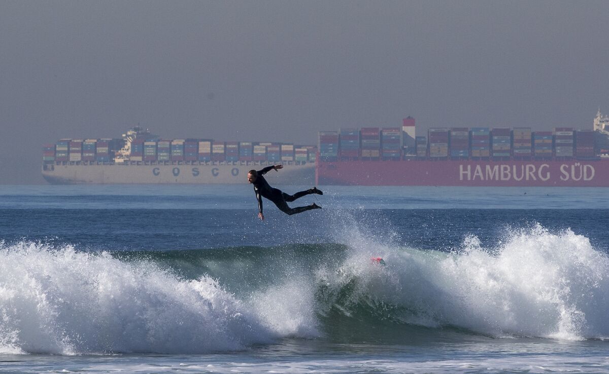 A surfer leaps off his board as container ships wait in line to be unloaded at the ports of L.A. and Long Beach.