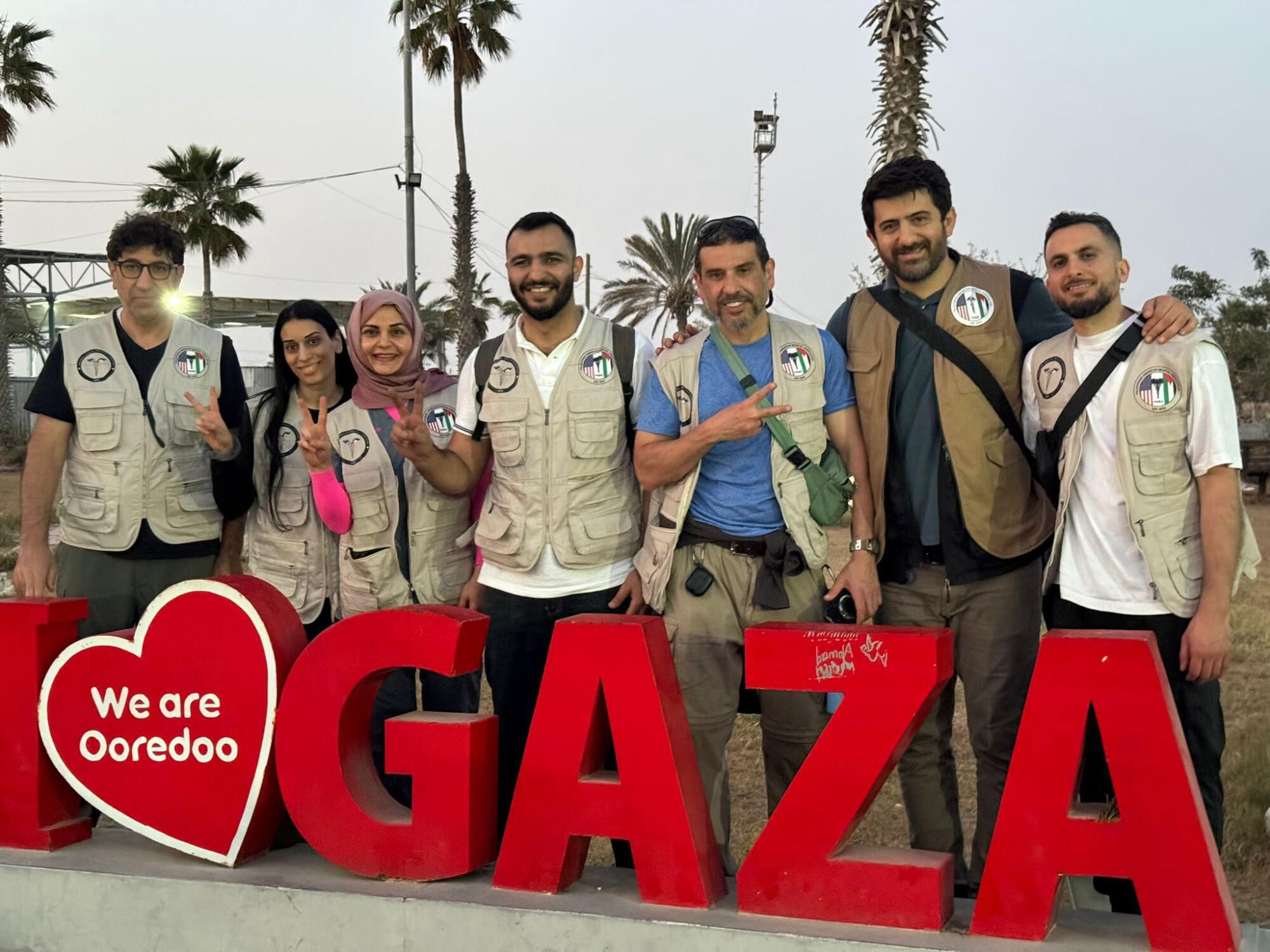 A group of medical workers in vests pose in a "I (heart) Gaza" sign.