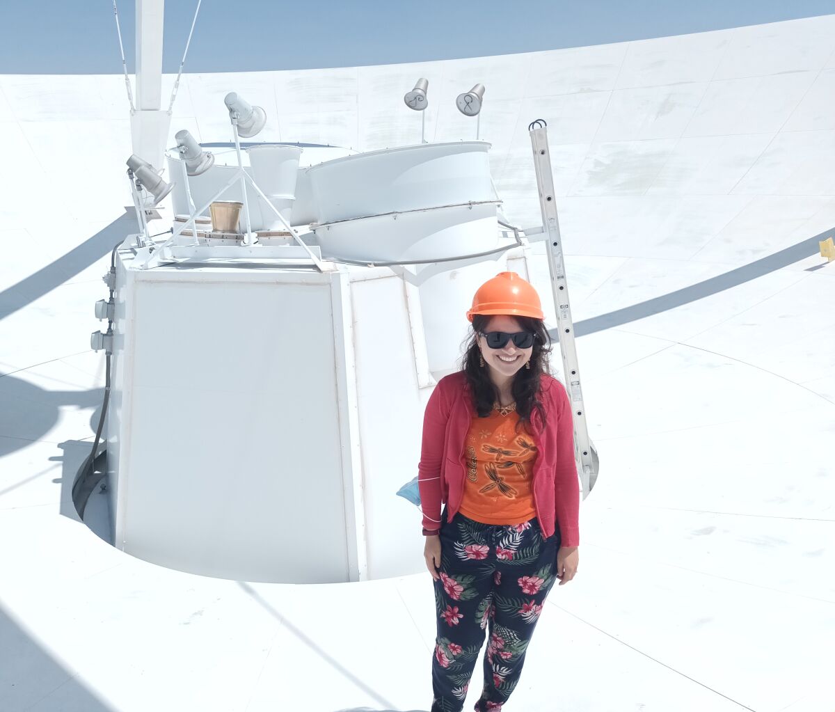 Sofía Rojas stands atop a large white receiver wearing sunglasses and a hard hat