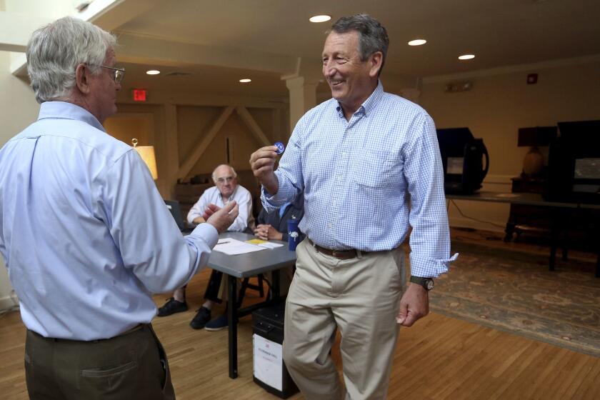 Poll volunteer Tom Spain hands out stickers to former Gov, Mark Sanford after he cast his own ballot at Alhambra Hall polling station Tuesday, June 12, 2018, in Mt. Pleasant, S.C. (Grace Beahm Alford/The Post And Courier via AP)