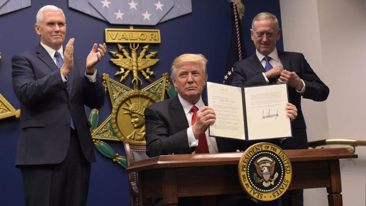 President Trump, flanked by Vice President Mike Pence, left, and Secretary of Defense James Mattis, shows his signature on executive orders signed Jan. 27.