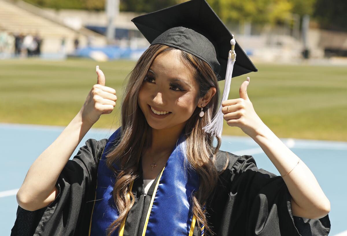 A woman in a cap and gown gives a thumbs-up on graduation day.