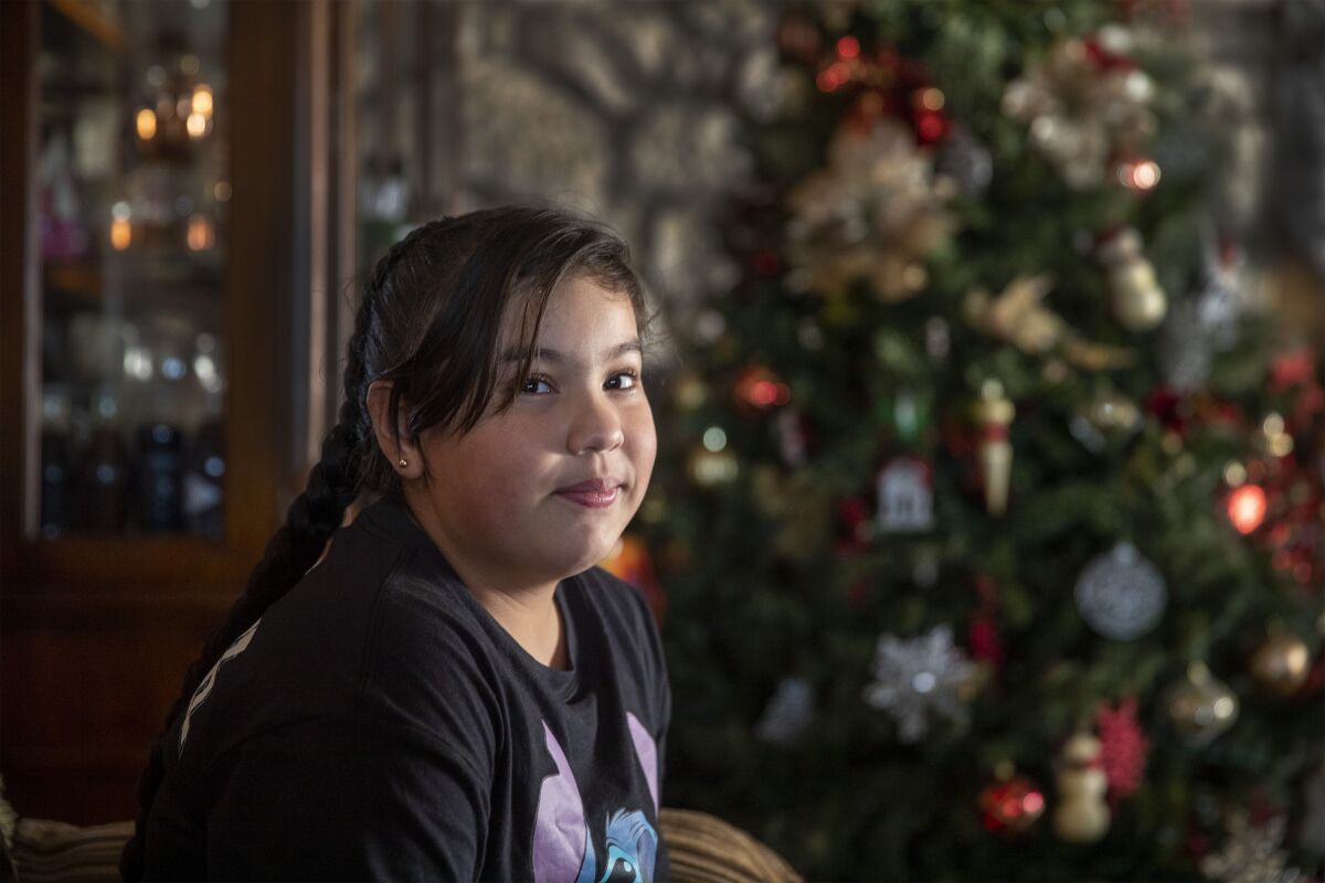 A girl sits in front of a Christmas tree in her home