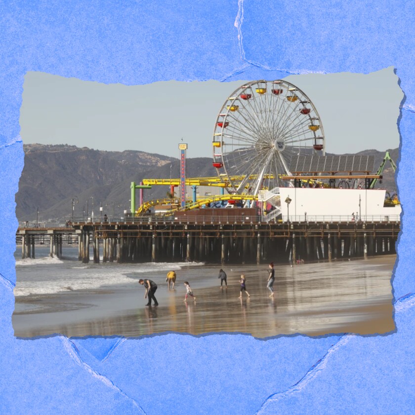 A pier with a Ferris wheel is seen from a distance.  People in the foreground walk on the beach.