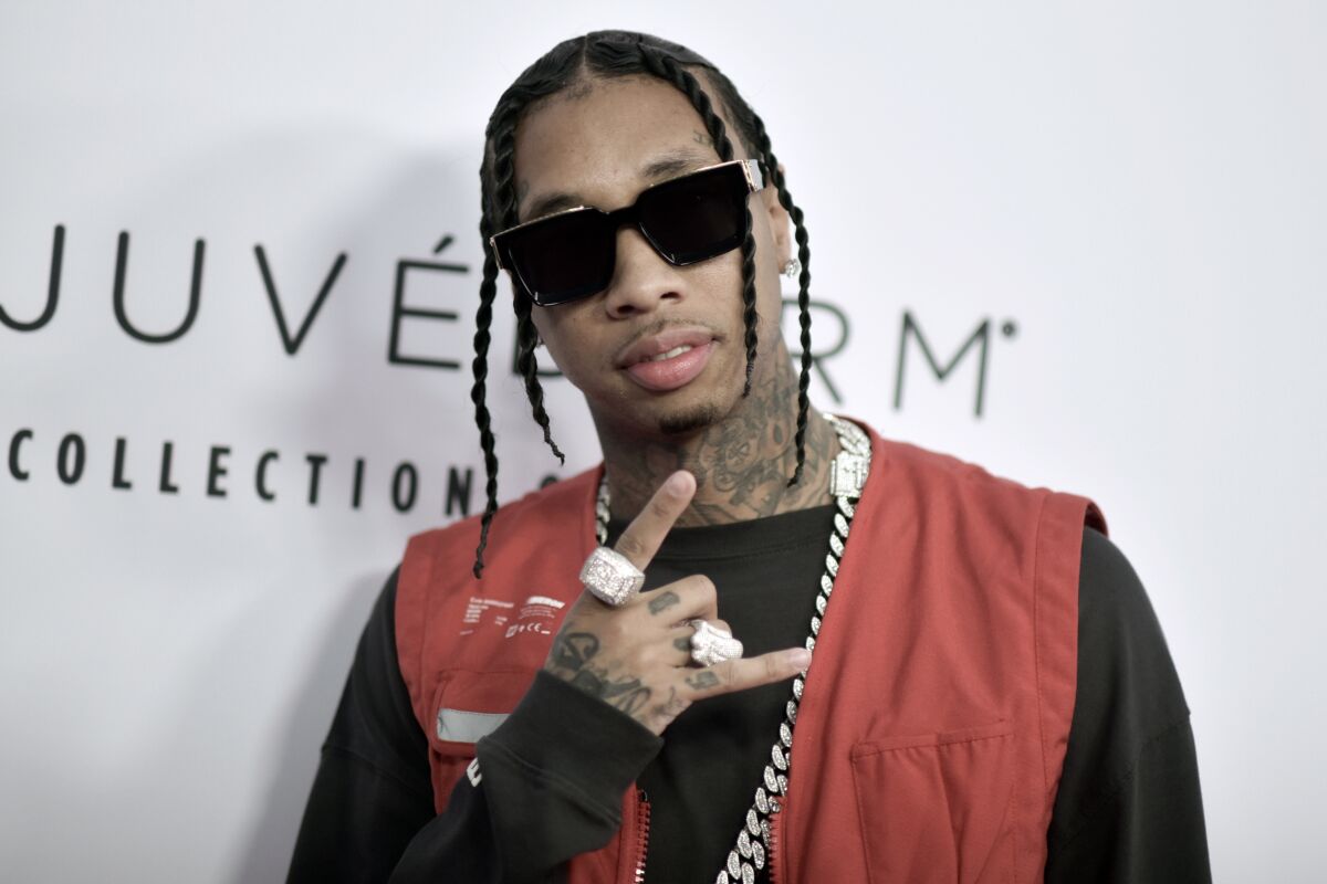 A man with neck tattoos, twists and sunglasses poses for a picture