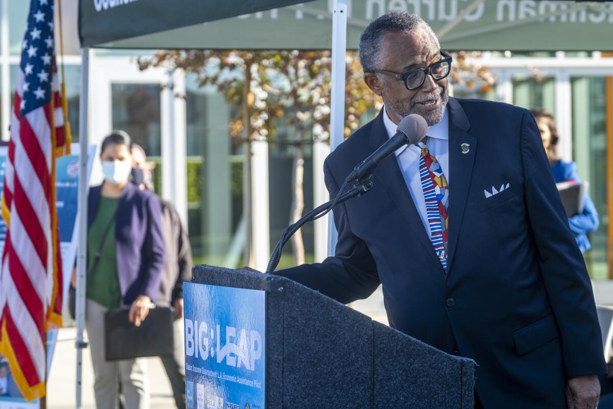 A man in a suit speaks into a microphone at a podium