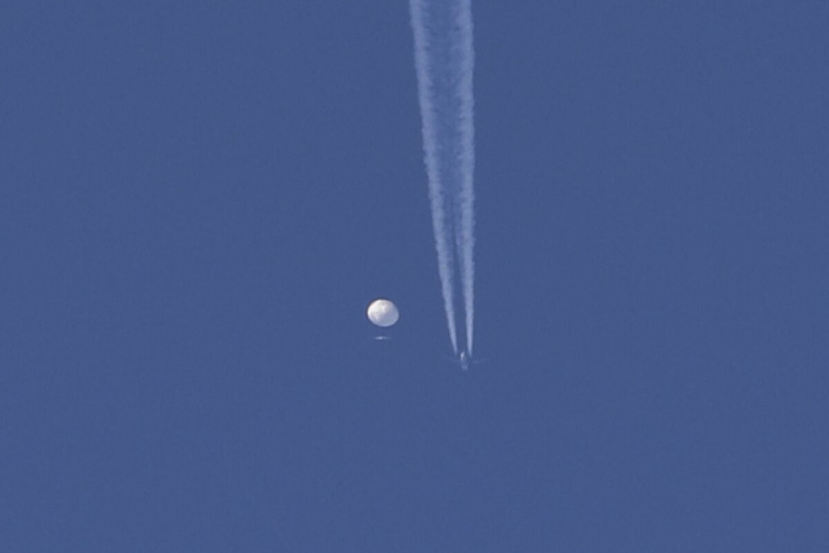 A large balloon drifts above the Kingston, N.C., area, with an airplane and its contrail near it.
