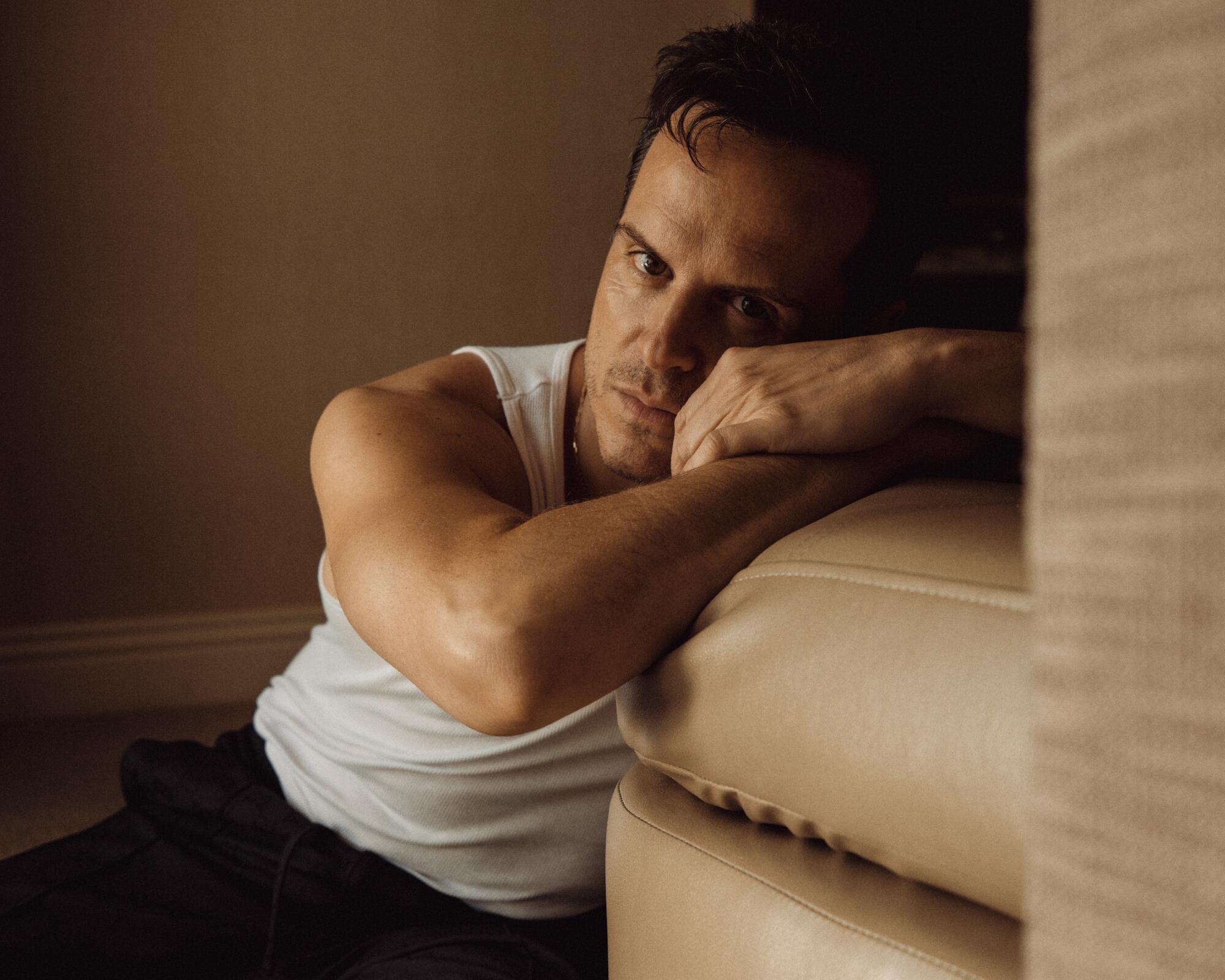 Andrew Scott wears a sleeveless shirt and leans his head on a couch for a portrait.
