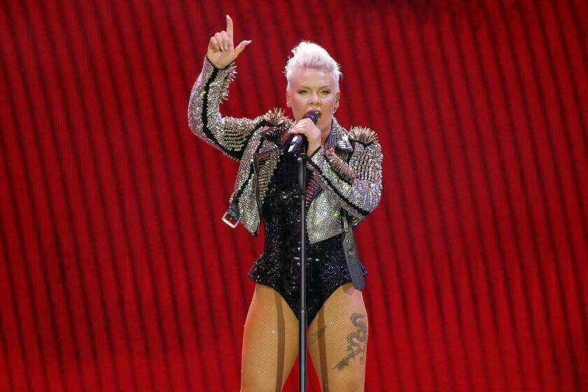 Pink in bedazzled leather jacket and leotard on a stage speaking into a microphone and holding her right arm up