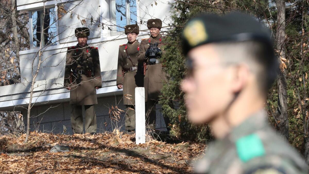 North Korean soldiers look to the south side of the Demilitarized Zone as a South Korean soldier stands guard.