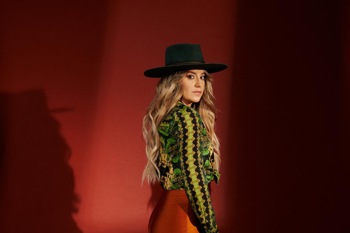 A woman with long blond hair in a black hat looks over her shoulder