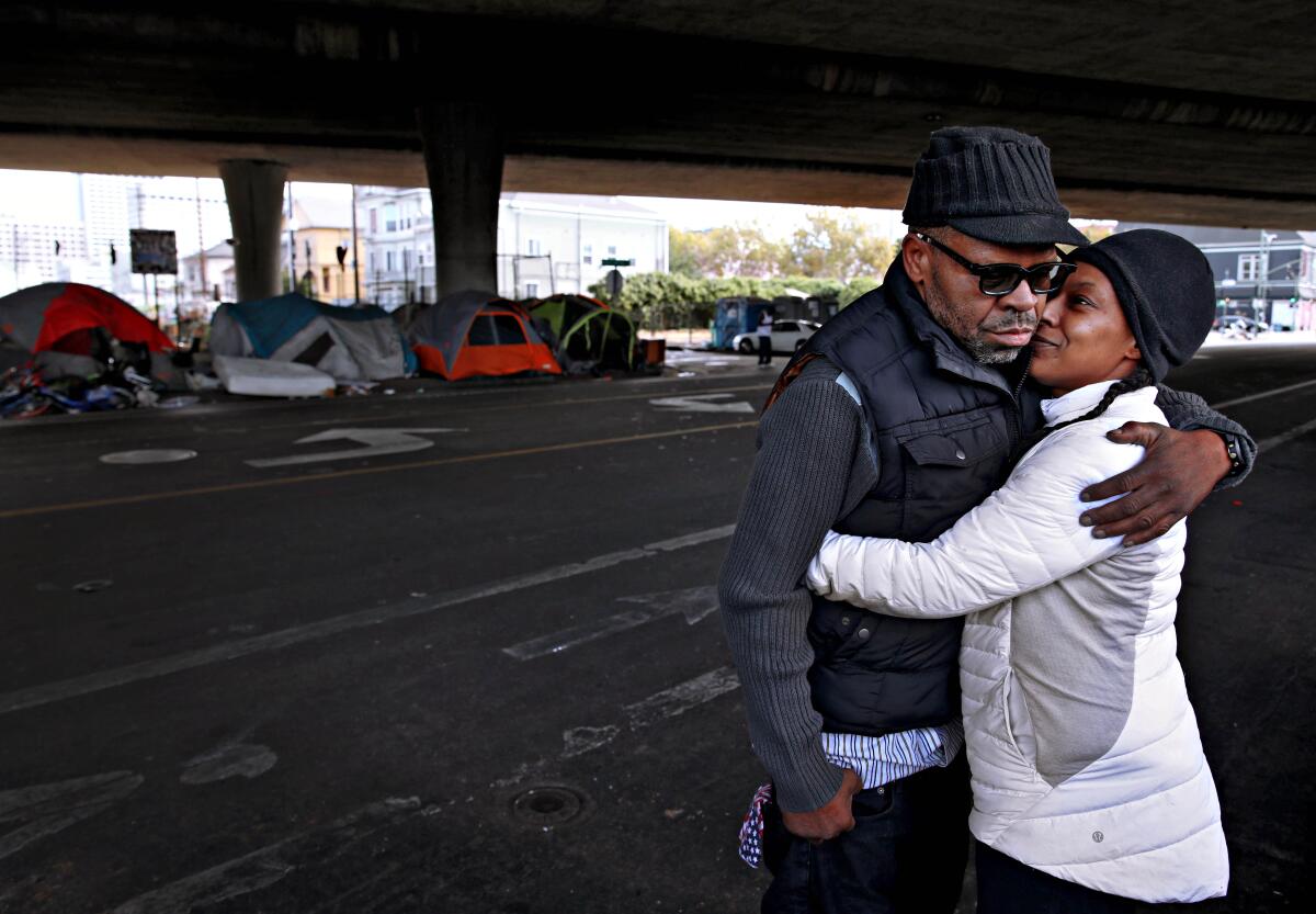 Two people embrace at a homeless encampment in Oakland.