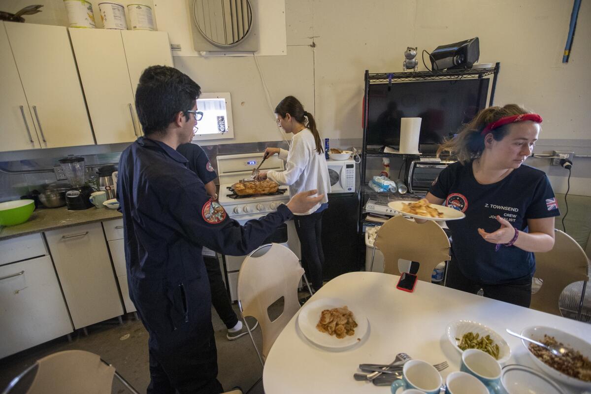 Zoe Townsend, right, serves lunch as Mariona Badenas-Agusti plates servings of 'Martian lasagna' a mix of pasta vegetables and freeze-dried meat in the crew hub. (Brian van der Brug / Los Angeles Times)