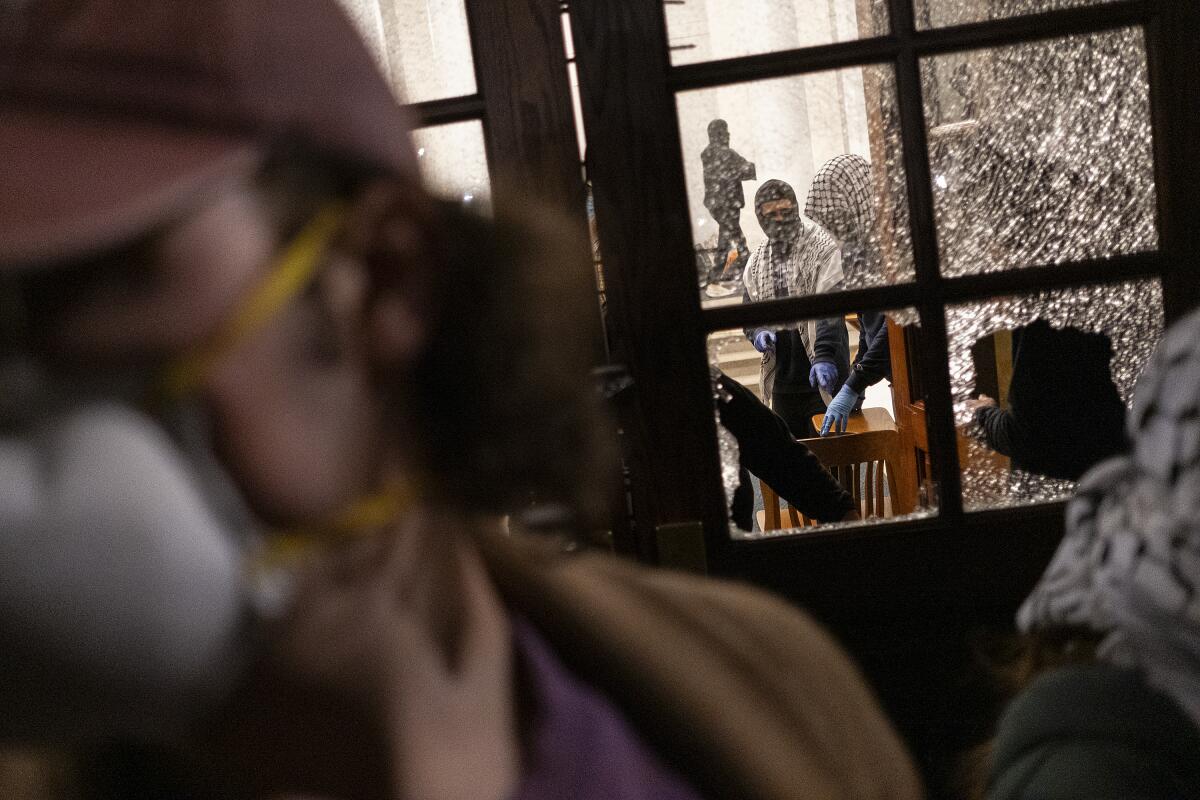 Protesters are seen through a shattered door glas 