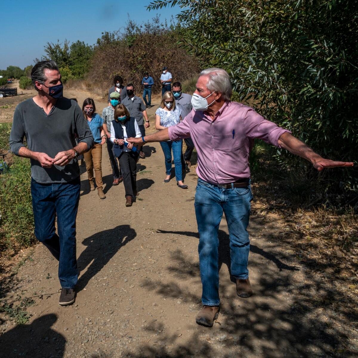 A masked Gov. Gavin Newsom walks along a trail with other walkers.