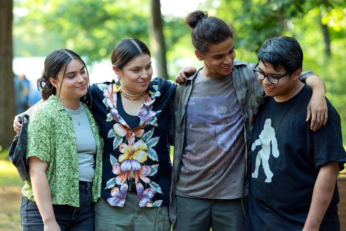 Two teen girls and two teen boys smile and put their arms around each other.