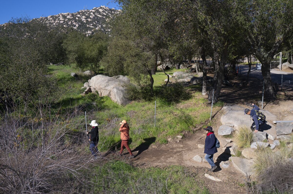 Hikers are seen from overhead walking up a trail among oak trees and boulders.