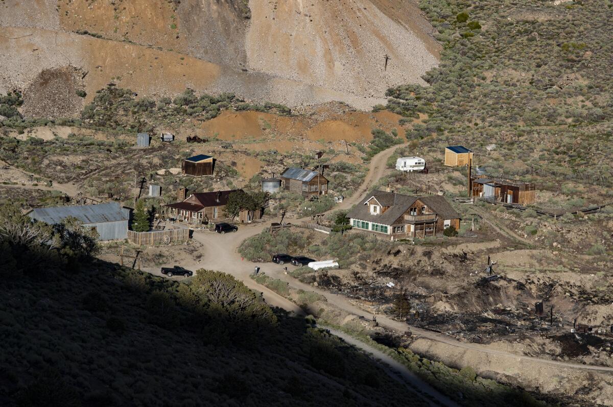 Rustic buildings on a brushy slope below mine tailings near the blackened ground where Cerro Gordo's  American Hotel burned.
