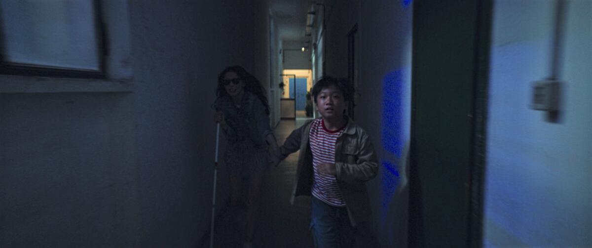A young boy leads a blind woman by the hand as they run down a hallway in the movie "Dark Glasses."