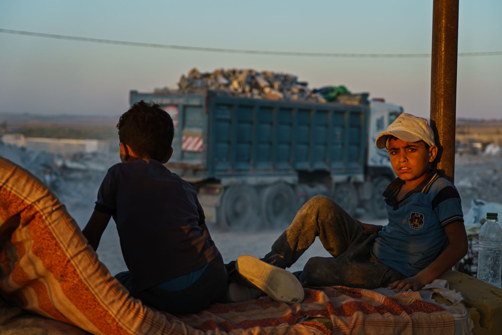 Children who work as laborers sit and rest as a truck brings in debris.    