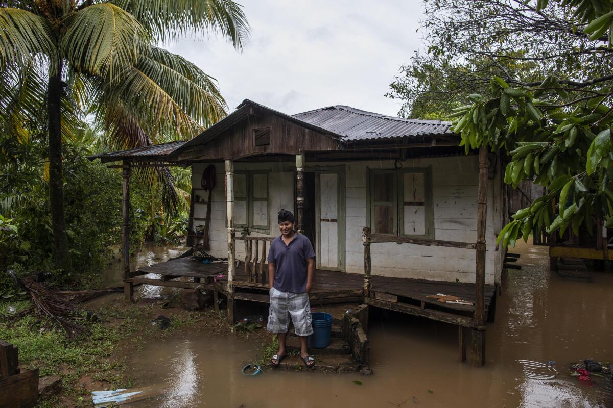 A man stands outside his house surrounded by floodwaters and tropical foliage.