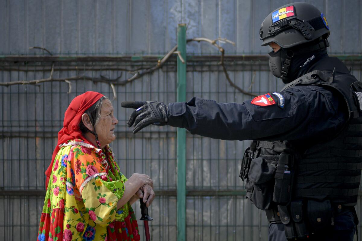 A riot police officer gestures while trying to turn an elderly Romanian Roma woman away