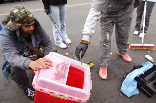 Samson Tafolo and Crushow Herring dispose of a needle they found on the sidewalk.