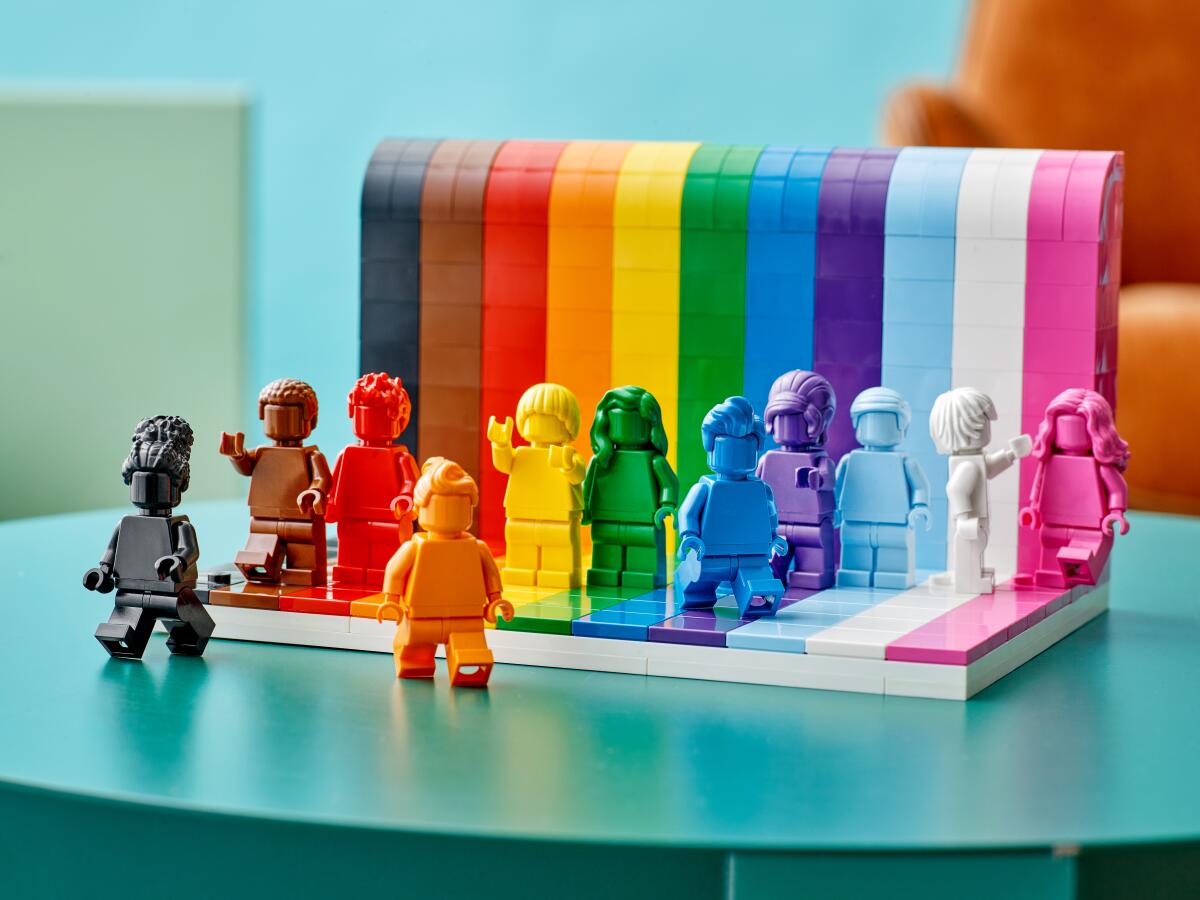 Various rainbow-colored Lego figurines standing on a Lego stage, on a blue table