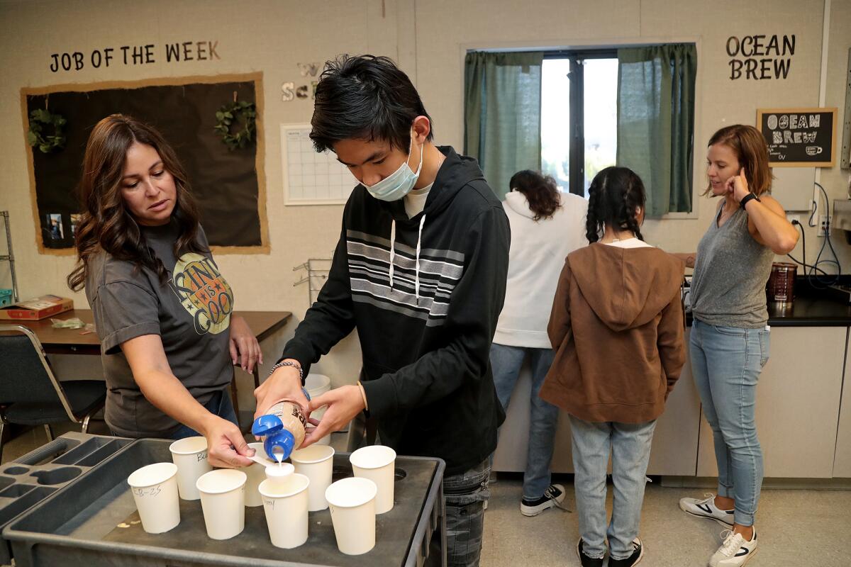Teacher's aide April Lancaster, left, guides senior Kevin Luu, 18, in measuring coffee creamer.