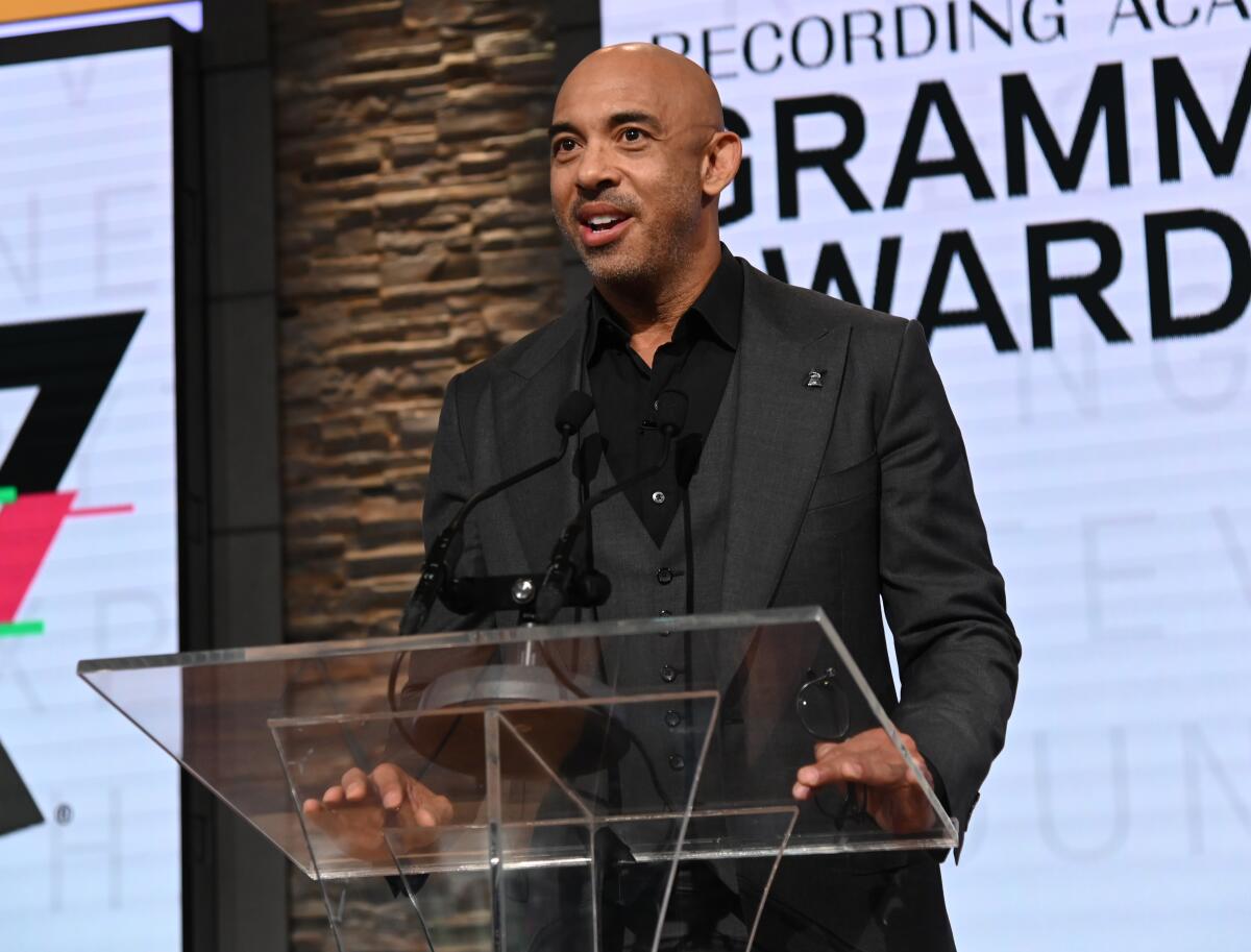 A man in a suit speaks at a clear podium onstage.