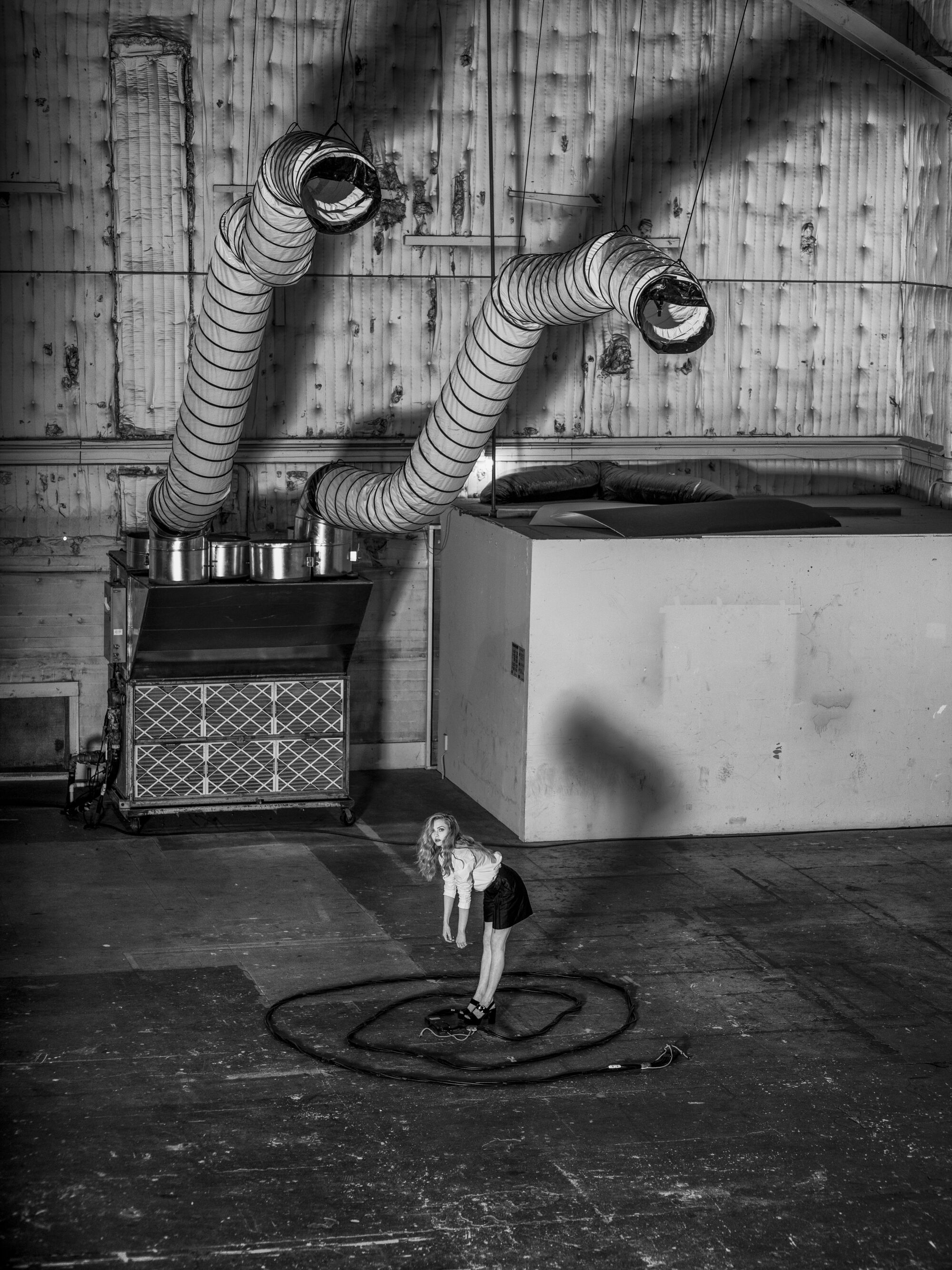 A woman stands in an empty warehouse surrounded by a spiral of cables